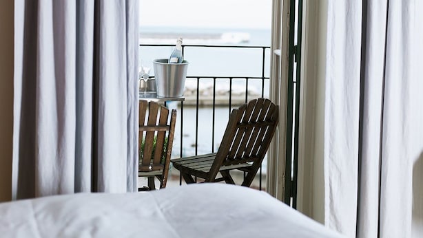 Un balcone con vista sul mare, un tavolo con un secchio e due sedie di legno.