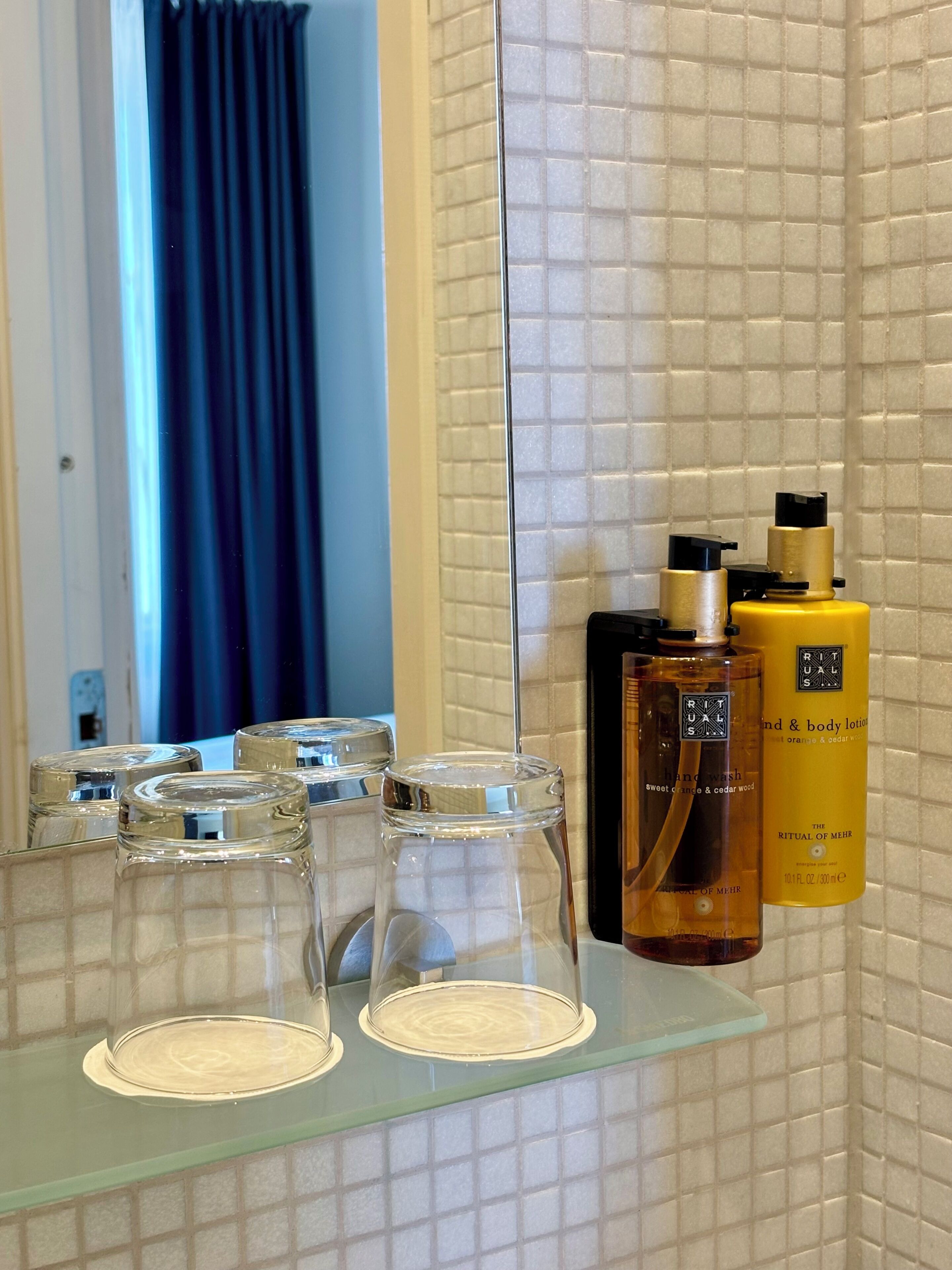 A bathroom with a glass shelf holding two bottles of lotion and a glass container.