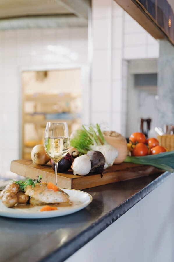 A kitchen counter with a glass of white wine, a plate of food, and various vegetables. - Maritim Hotell och Krog (Simrishamn)