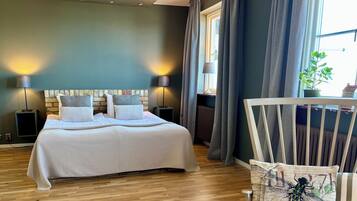 A bedroom with a large bed, two bedside lamps, a radiator, and a window with curtains.