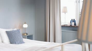 Un dormitorio con cama, mesita de noche, lámpara y ventana con cortinas.