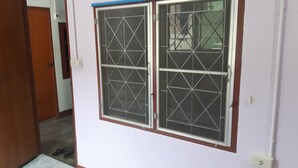 A room with a door leading to a hallway, a window with metal bars, and a white wall. - Canaan Guesthouse (Kanchanaburi)