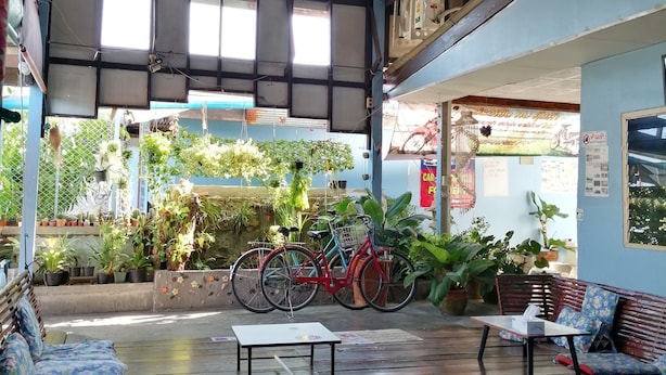 A spacious indoor area with a wooden floor, a ceiling fan, and a seating area with benches and a table. - Canaan Guesthouse (Kanchanaburi)