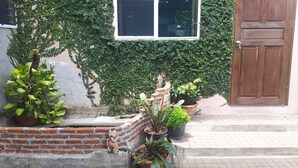 A brick wall with a window and a door, surrounded by greenery and potted plants. - Canaan Guesthouse (Kanchanaburi)