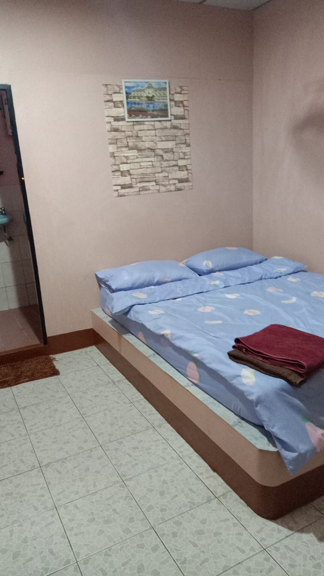 Un dormitorio con una cama, un tapete pequeño, un cuadro en la pared y suelo de baldosas.