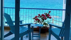 A balcony with a view of the ocean, featuring two blue chairs, a small table, and a potted plant with pink flowers. - Blue Anchor Lodge & Cafe-Binh Ba Island (Nam Cam Ranh)