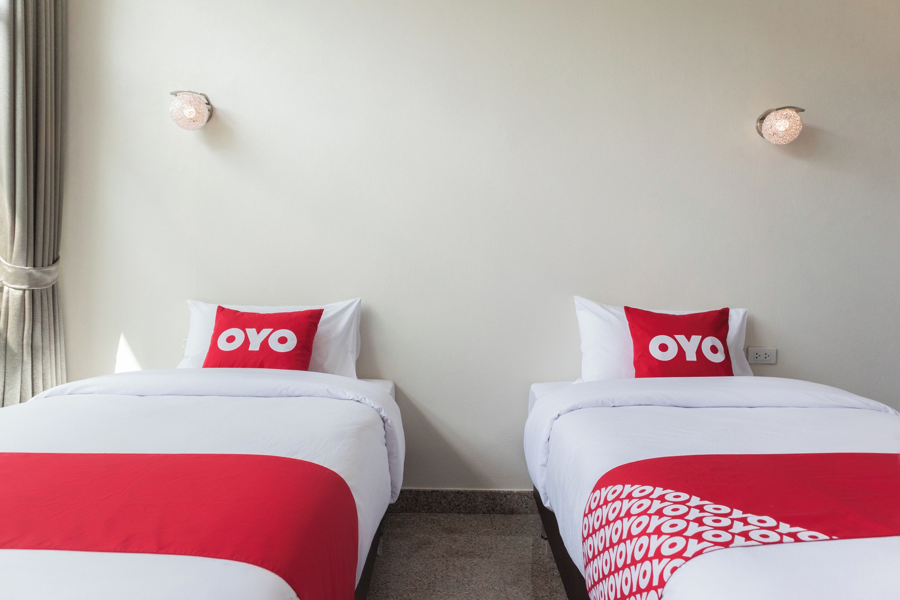 A hotel room with two beds, each with white bedding and red accents, including pillows and a blanket.