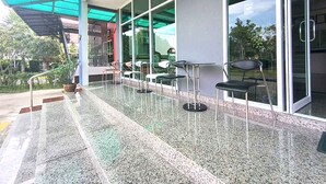 Un espacio al aire libre cubierto con sillas y mesas, ventanas amplias y vistas a zonas verdes.