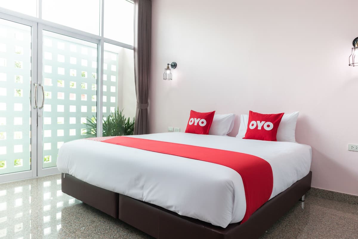 A hotel room with a large bed, a red and white bedspread, and a view through a glass door.