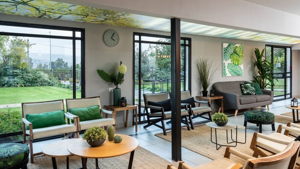A spacious living area with large windows, a sofa, chairs, and a coffee table. - Erettz Dafna Travel Hotel (HaGalil HaElyon)