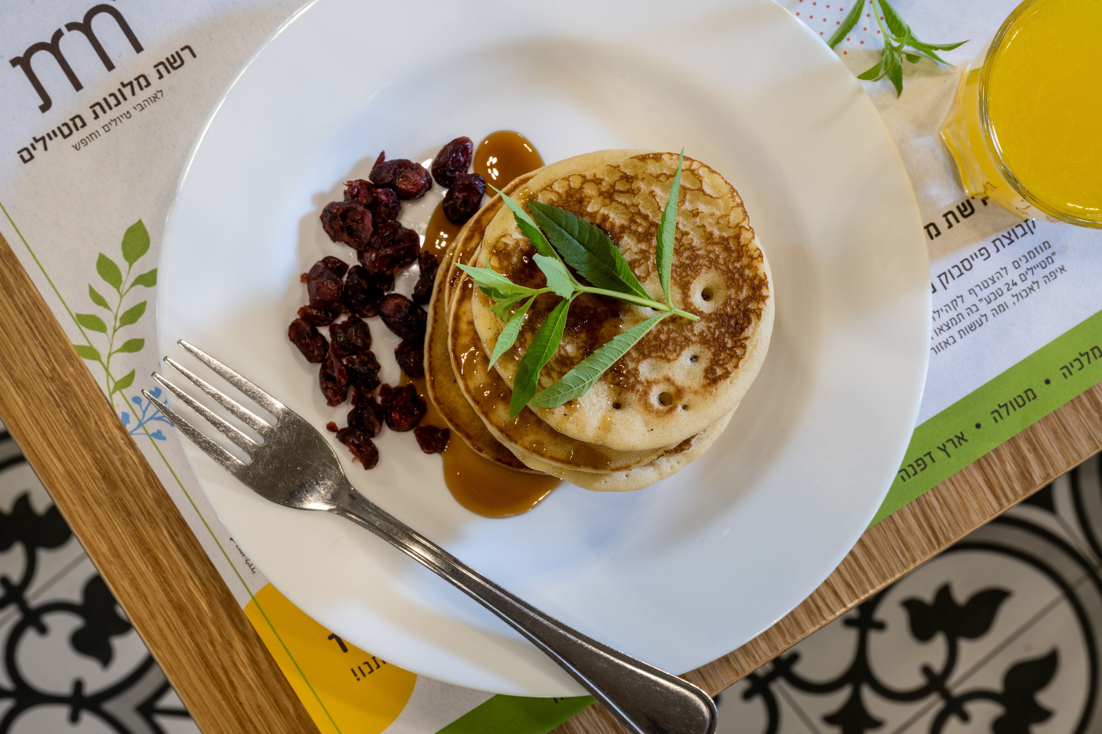 A plate with pancakes, syrup, and raisins on a table with a menu.