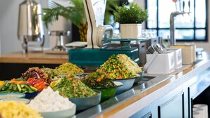 A buffet with various dishes, including salads and grains, arranged on a counter with a water dispenser and a potted plant in the background. - Erettz Dafna Travel Hotel (HaGalil HaElyon)
