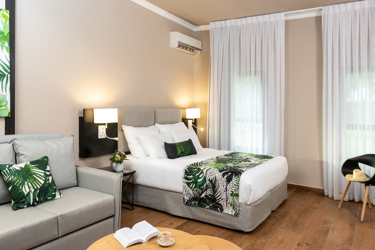 Ein Hotelzimmer mit Bett, einer Couch, einem Couchtisch mit offenem Buch und einem Sessel.