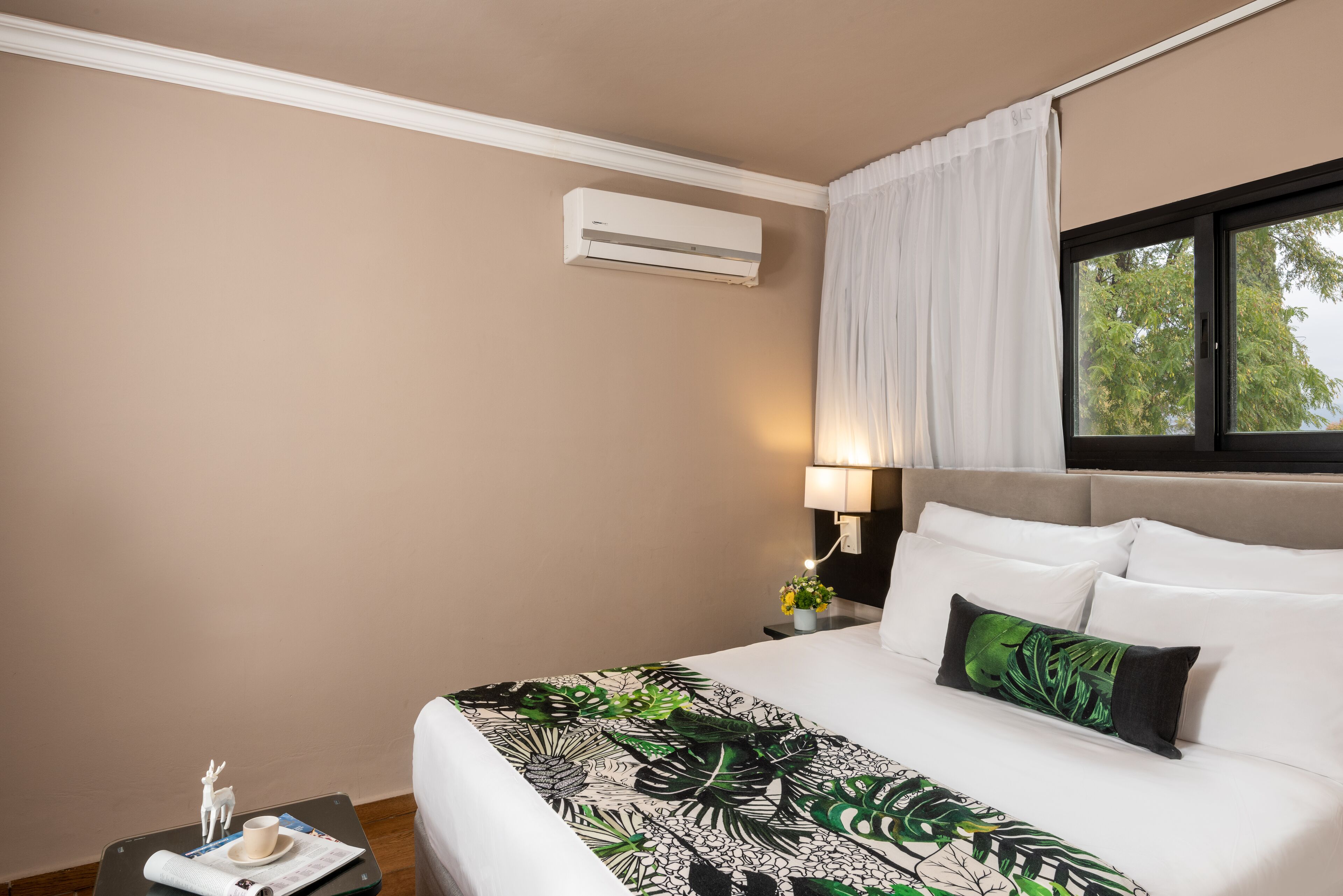 A hotel room with a bed, a nightstand, a lamp, and an air conditioning unit.