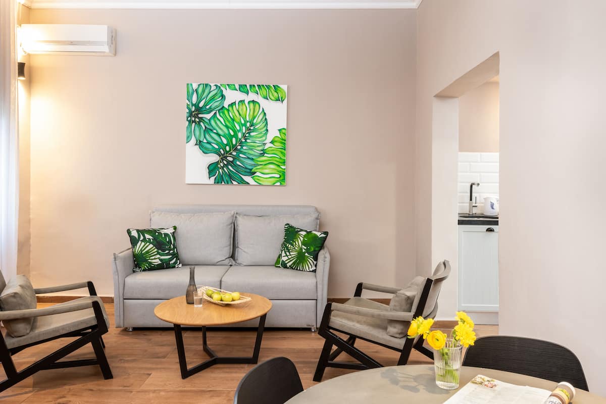 Ein Wohnzimmer mit grauem Sofa, zwei Sesseln, einem Couchtisch und einer Küche im Hintergrund.