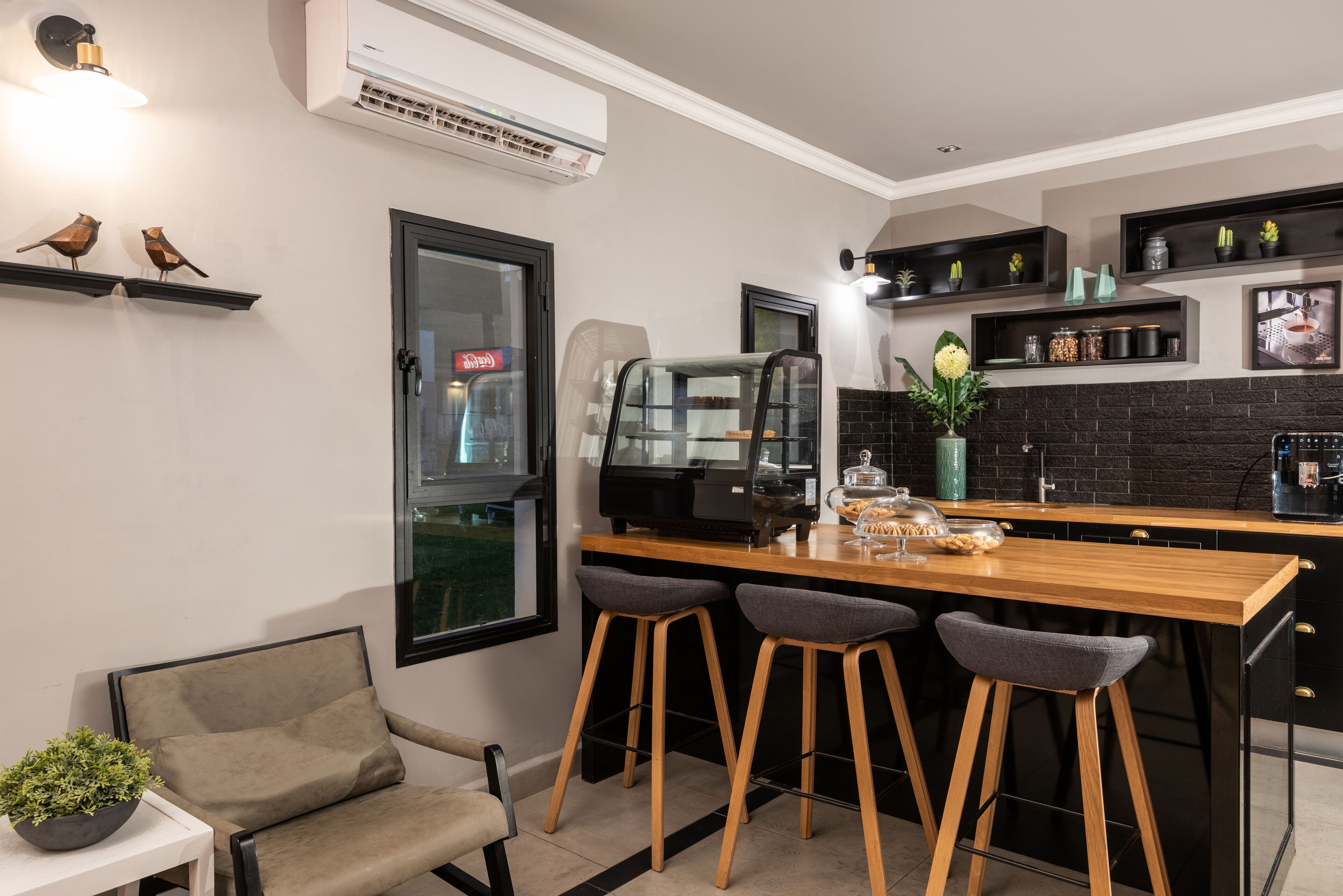 Een moderne keuken met een houten bar, twee barkrukken, een koelkast en een raam.