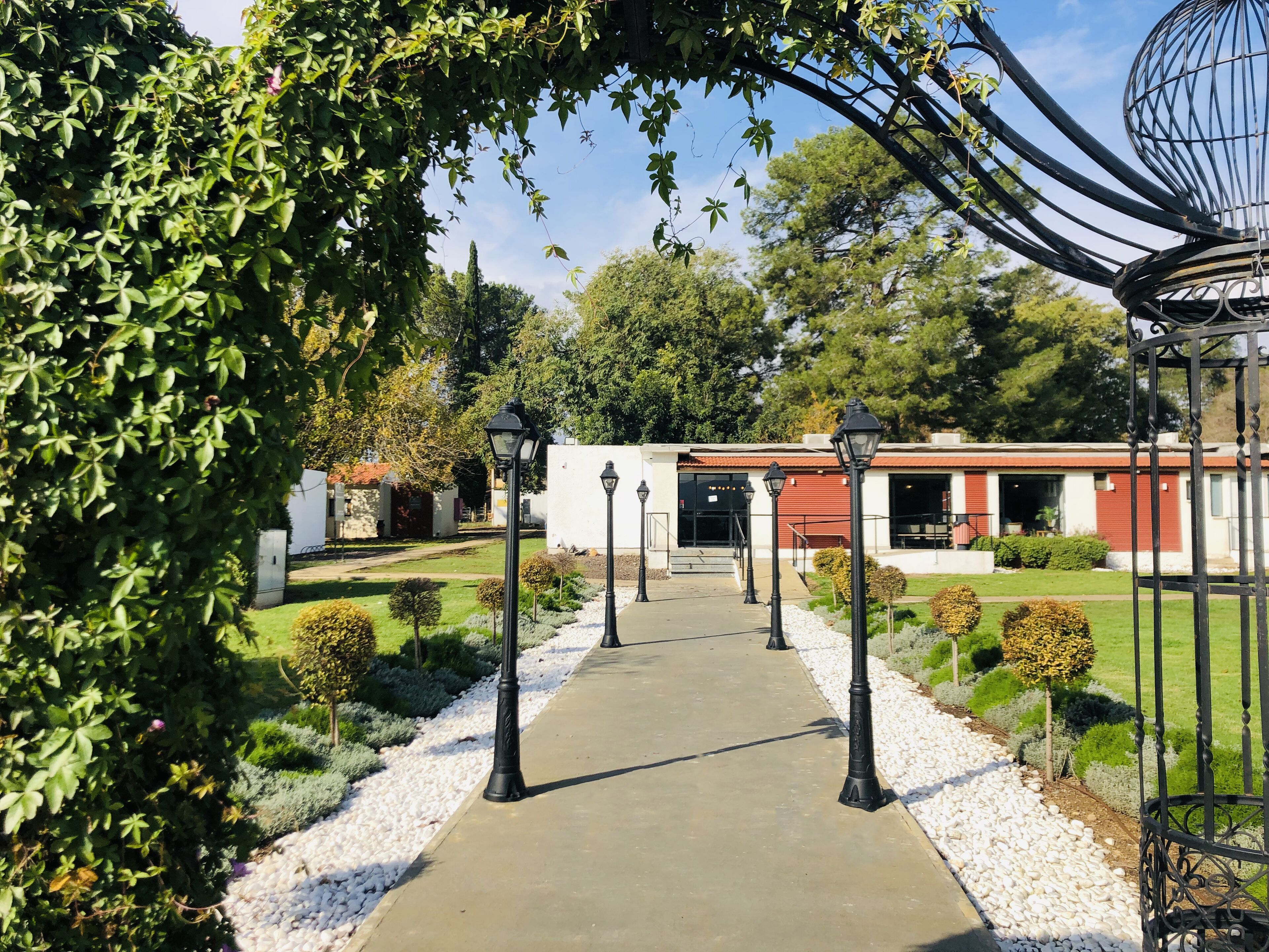 A pathway leading to a building with a red roof, surrounded by greenery and white gravel.