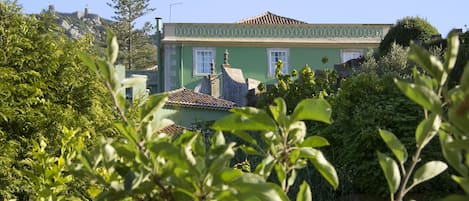 A green building with a tiled roof, surrounded by lush greenery.