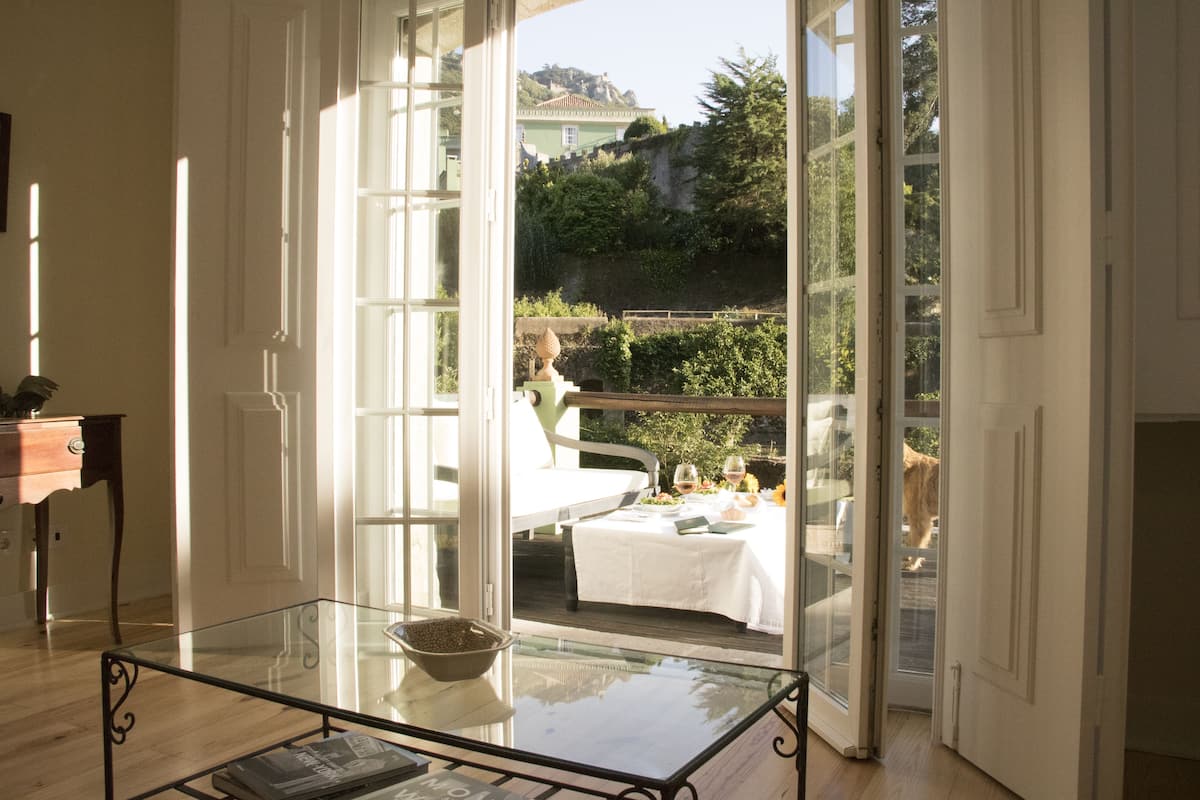 Una habitación con una mesa de vidrio, un mantel blanco y vistas a un comedor exterior.