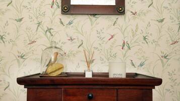 A wooden console table with a glass birdcage, a reed diffuser, and a candle labeled "aroma botanical" against a wallpaper with a bird and plant pattern.