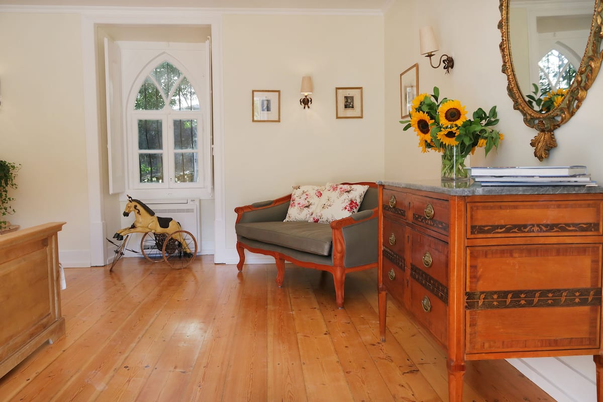 Una habitación con piso de madera, un caballo balancín de madera, un sofá con cojines estampados, un aparador de madera con cajones y un espejo grande.