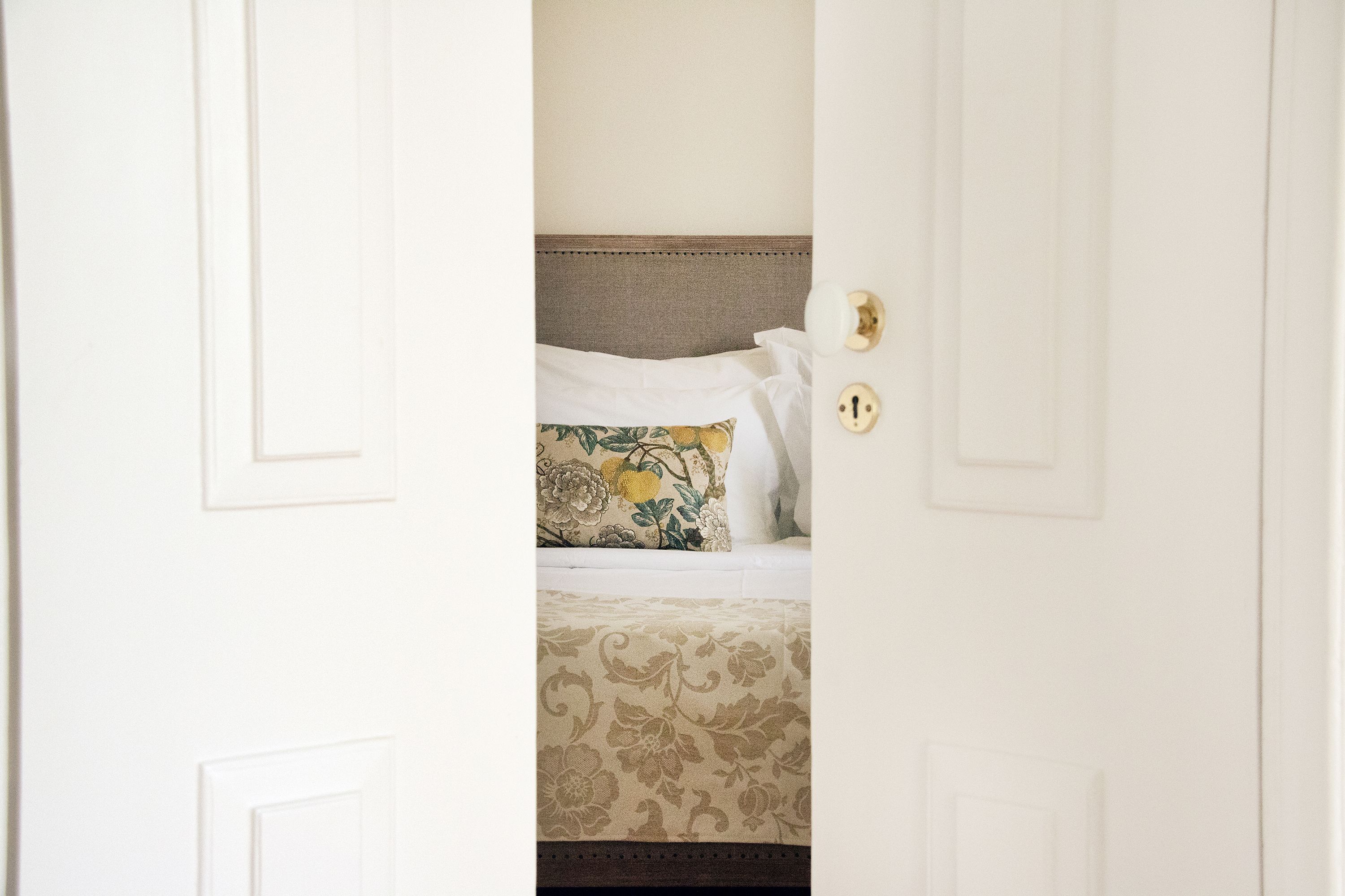 A hotel room with a bed featuring a floral-patterned bedspread and a decorative pillow.