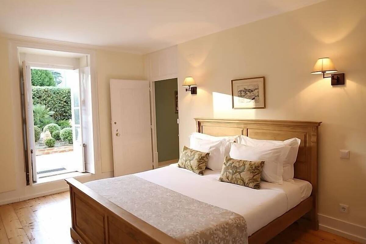 Un dormitorio con una cama de madera, dos lámparas fijadas a la pared, una puerta que da a un balcón y un cuadro enmarcado en la pared.