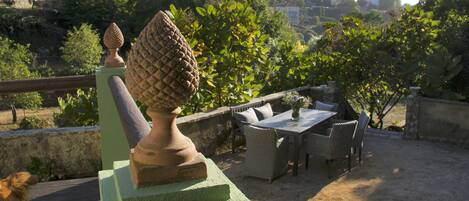 A patio area with outdoor furniture, a decorative urn, and a view of a hillside with buildings.