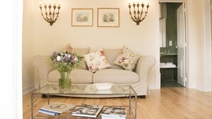 A living room with a beige sofa, floral cushions, a glass coffee table with books, a vase with flowers, and wall-mounted candelabras. - Casa Holstein Quinta de São Sebastião (Sintra)