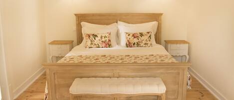 A bedroom with a wooden bed, floral bedding, two bedside lamps, and a bench.