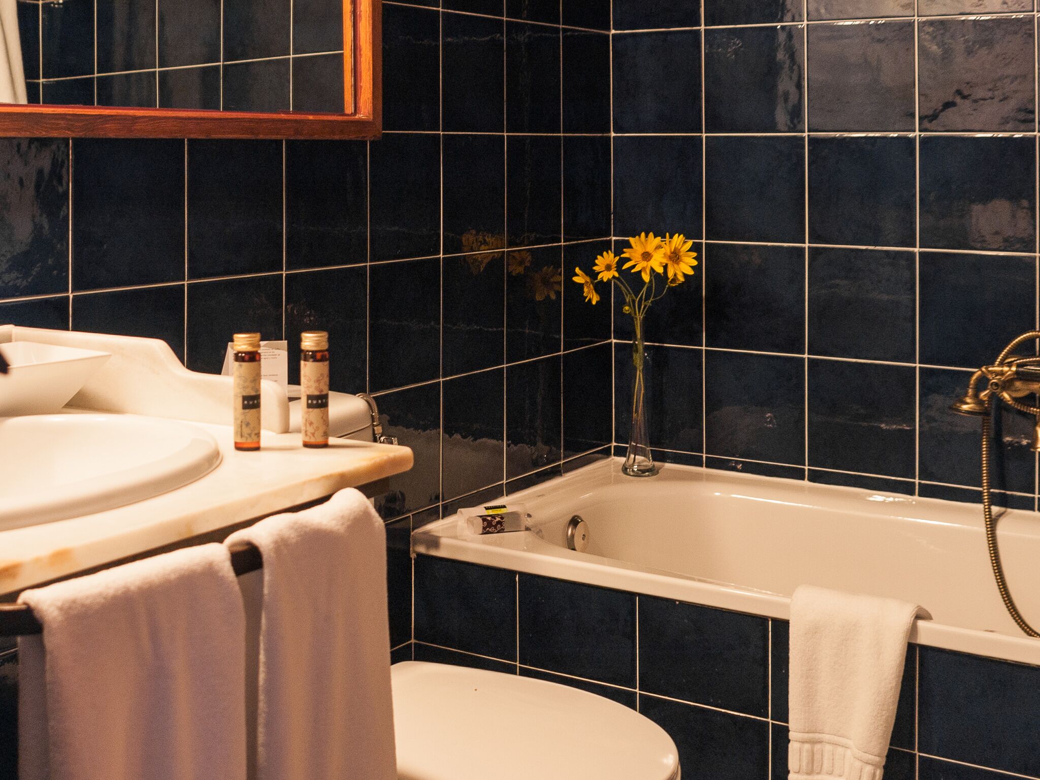 Une salle de bain avec des carreaux bleu foncé, une baignoire blanche, un lavabo blanc et un miroir au-dessus du lavabo.