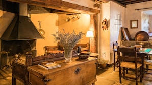 Une pièce rustique avec une commode en bois, un vase de fleurs séchées, une lampe et une table en pierre.