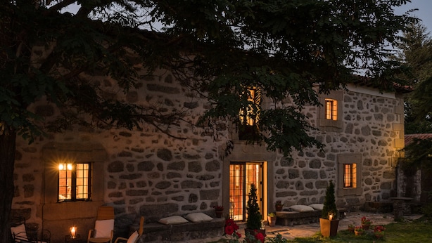 Un bâtiment en pierre doté d’un jardin, d’un espace extérieur aménagé pour s’asseoir et d’un intérieur éclairé.