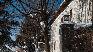 Une cour enneigée, avec un mur de pierre, un arbre et un bâtiment orné d’une lanterne.