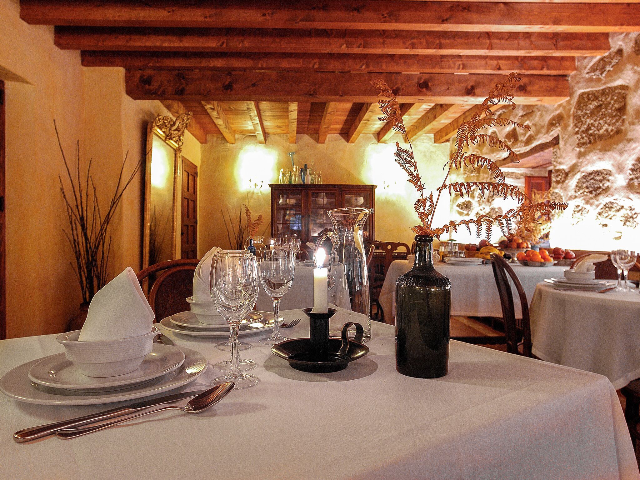 A dining table set with plates, cutlery, wine glasses, a candle, and a decorative vase.