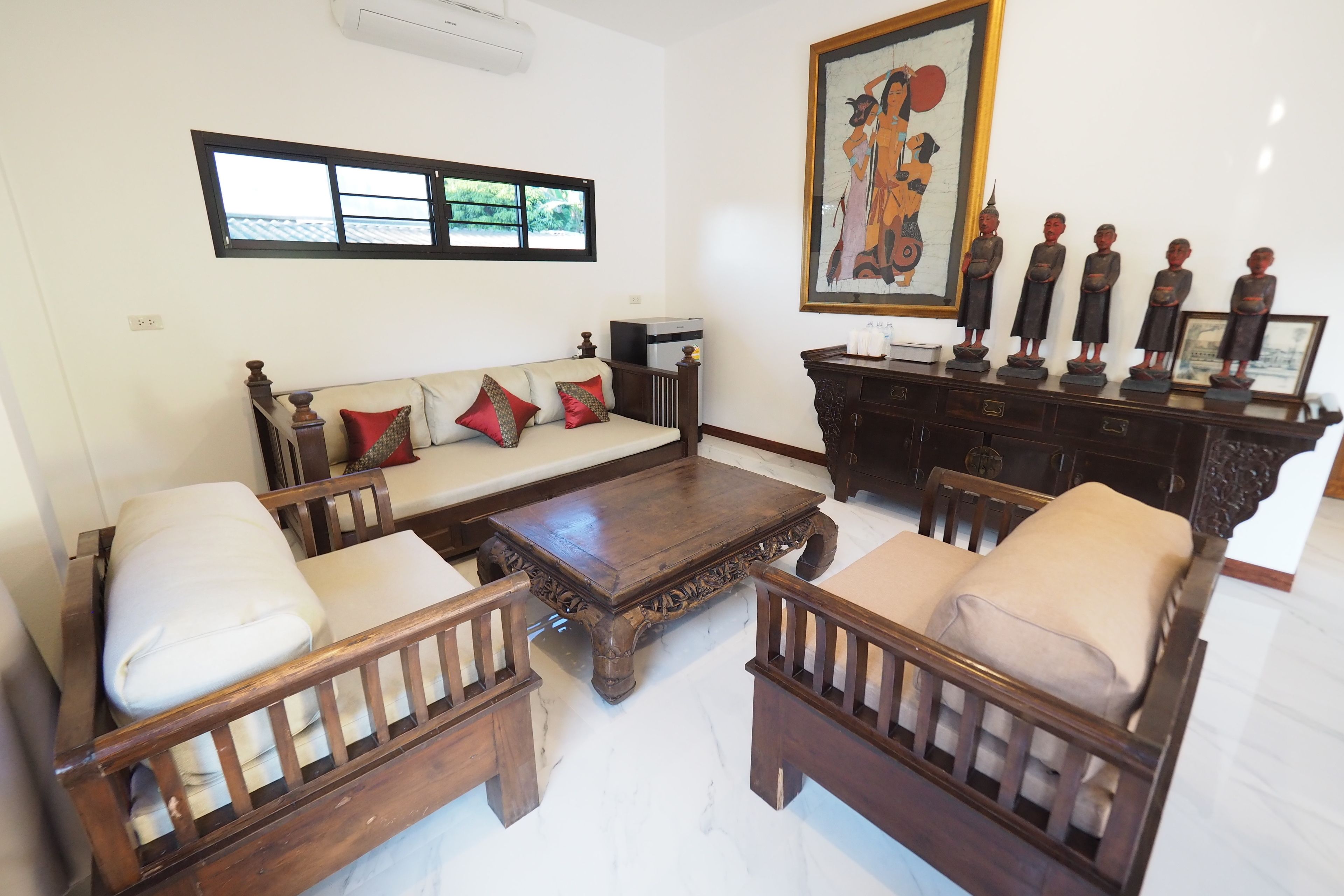 A living room with a sofa, two wooden chairs, a coffee table, a cabinet with figurines, and a painting on the wall.