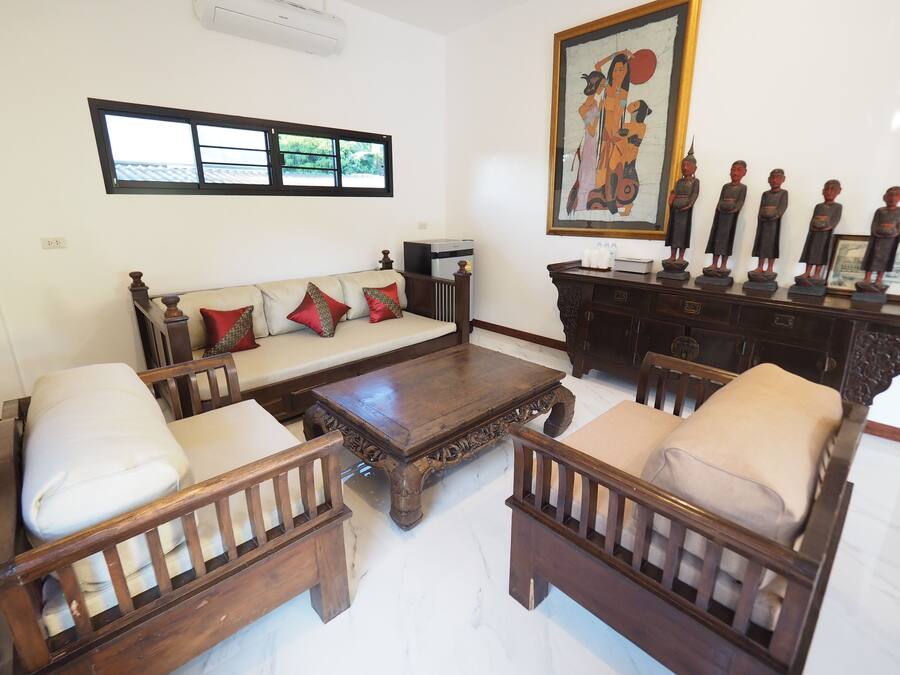 A living room with a sofa, two wooden chairs, a coffee table, a cabinet with figurines, and a painting on the wall.
