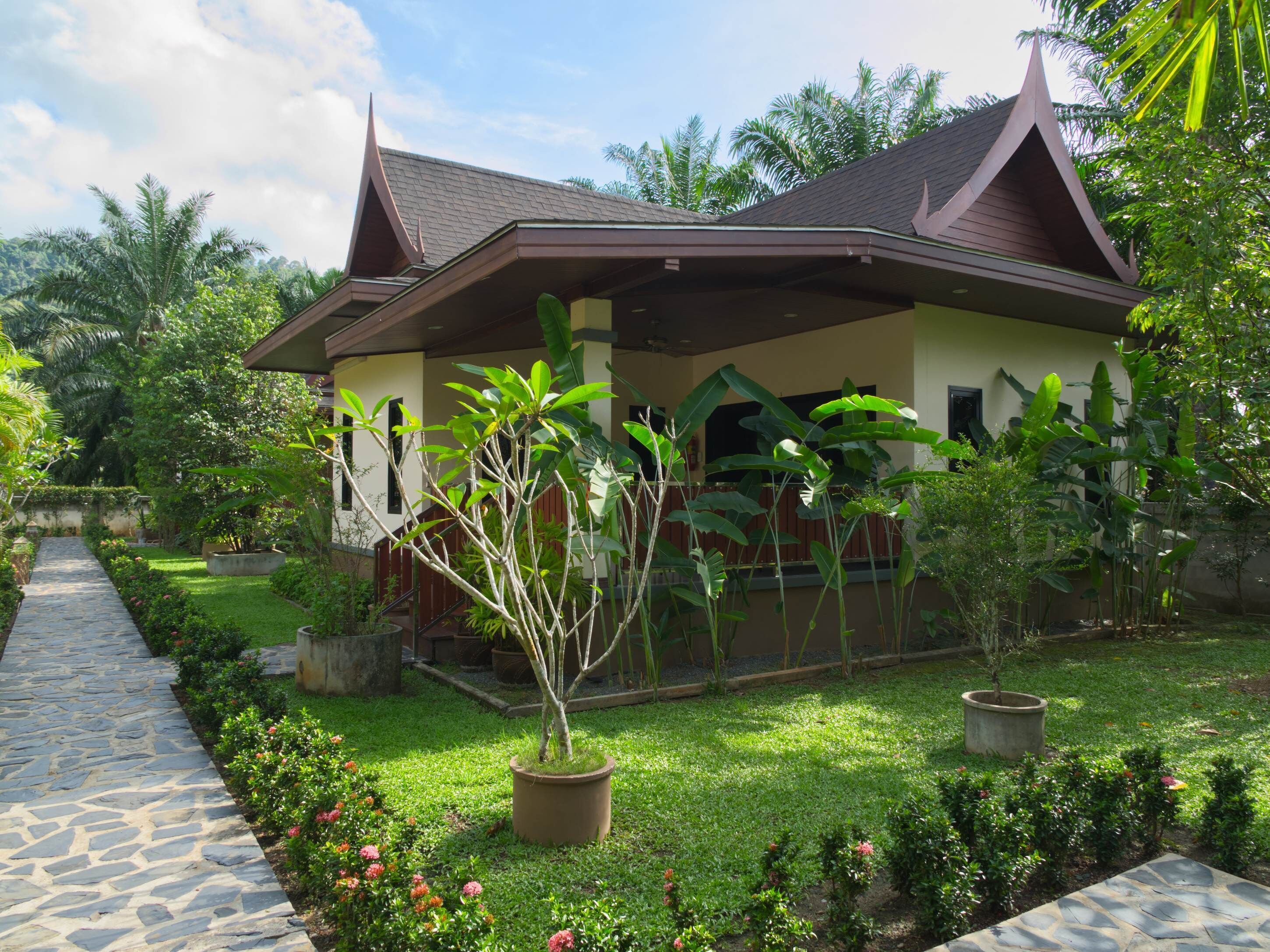 A traditional house with a sloped roof, surrounded by lush greenery and a stone pathway.