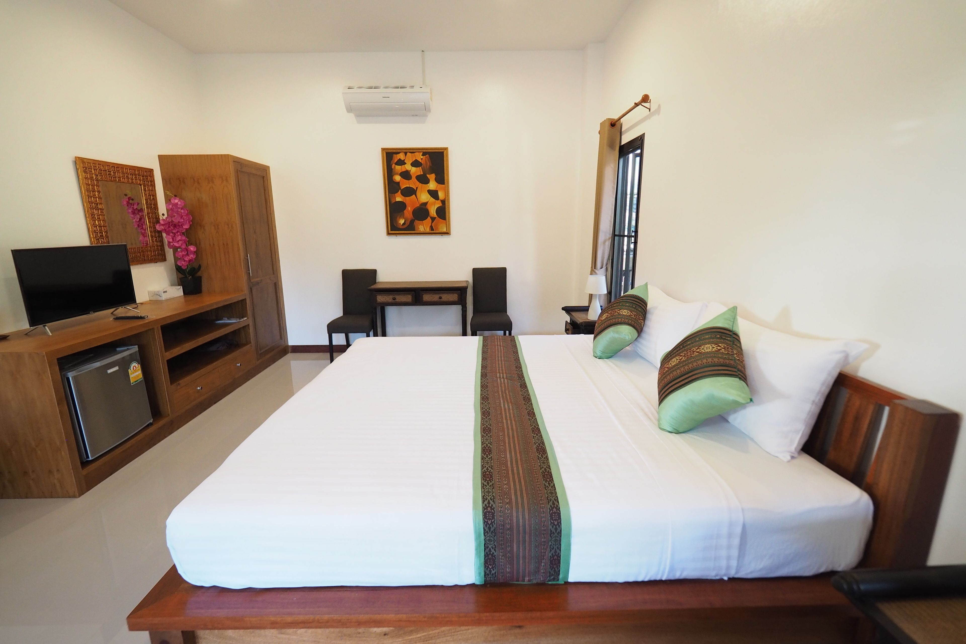Habitación de hotel con una cama grande, un escritorio con dos sillas, televisión, armario y un cuadro en la pared.