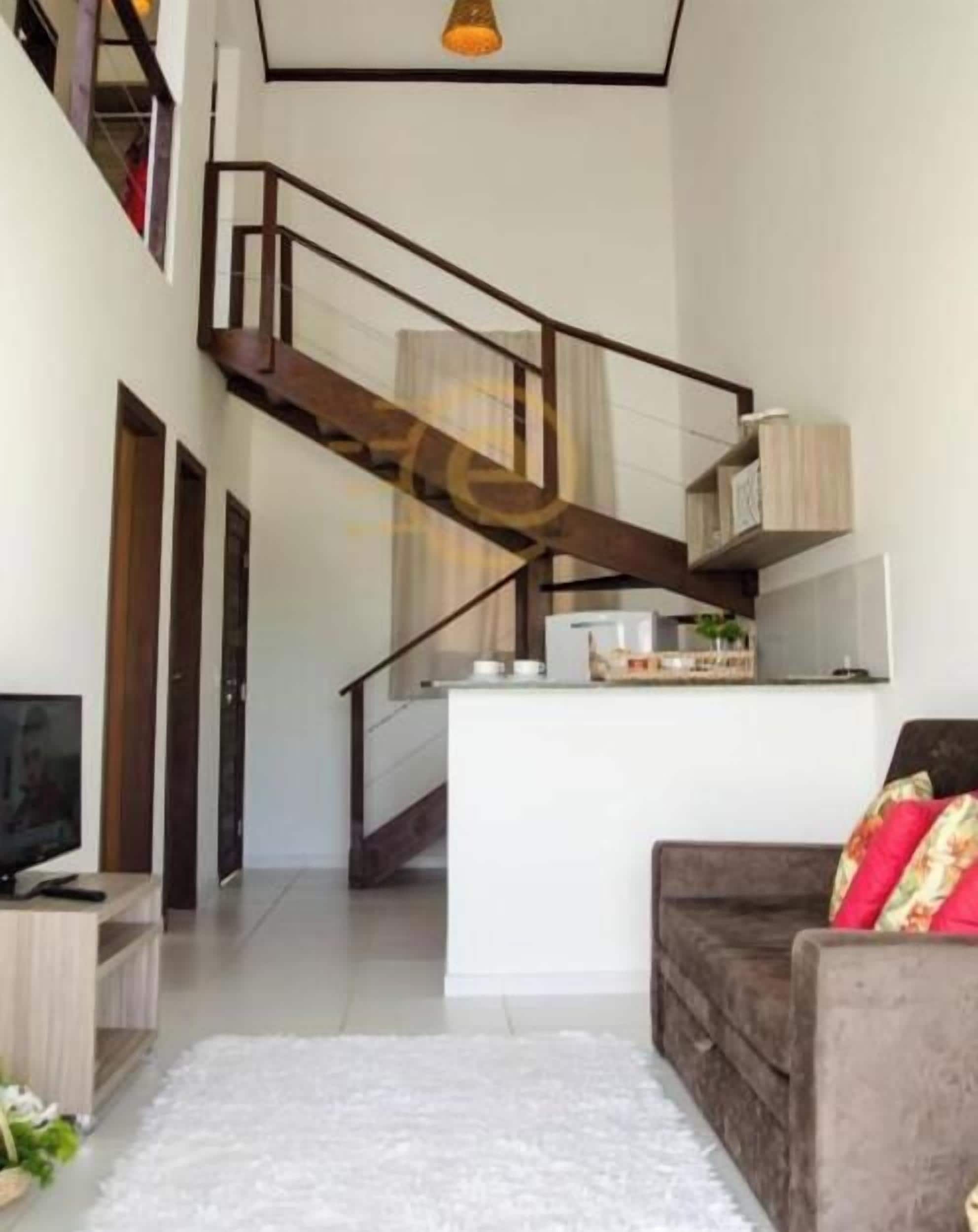 Decoração moderna com escada para um andar superior, TV de tela plana em um suporte de madeira e sofá com almofadas estampadas.
