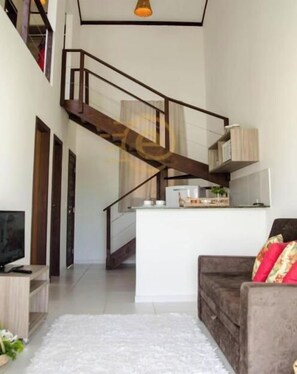 Un interior moderno con una escalera que sube a un nivel superior, un televisor de pantalla plana sobre un soporte de madera y un sofá con cojines estampados.