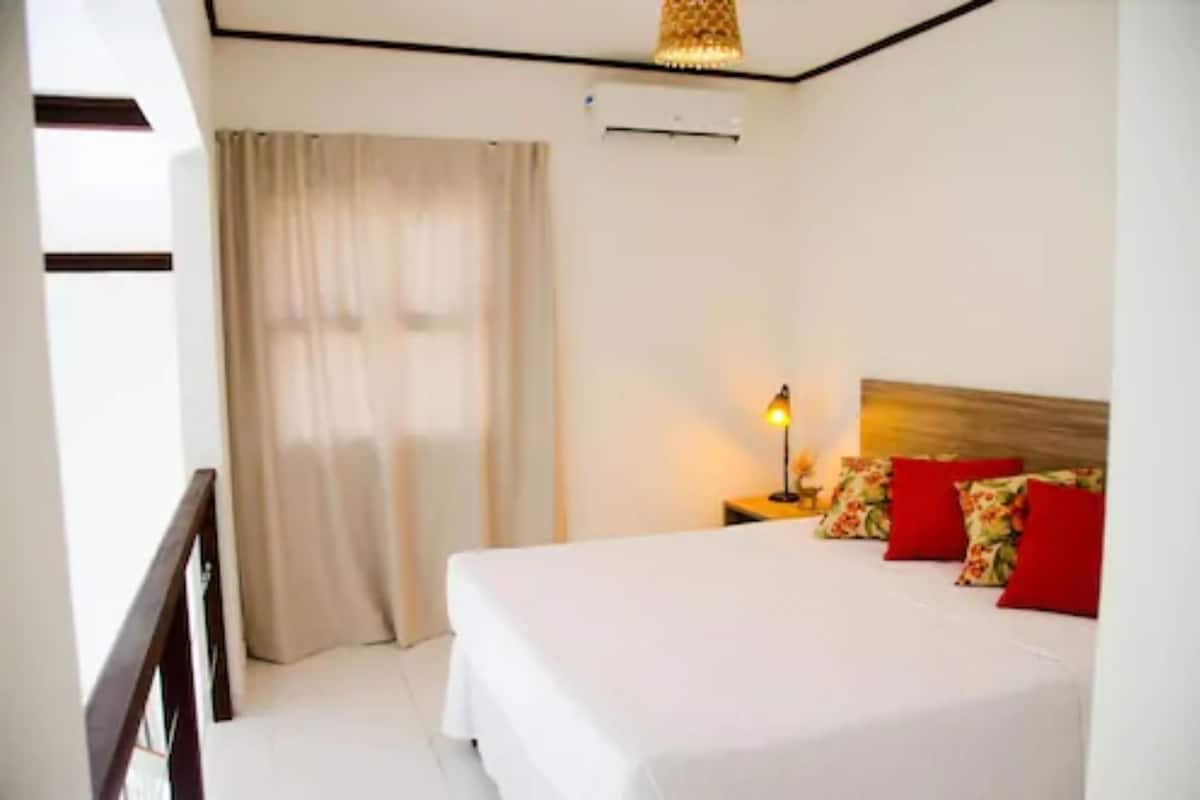 A hotel room with a bed, a nightstand, a lamp, and a window with curtains.