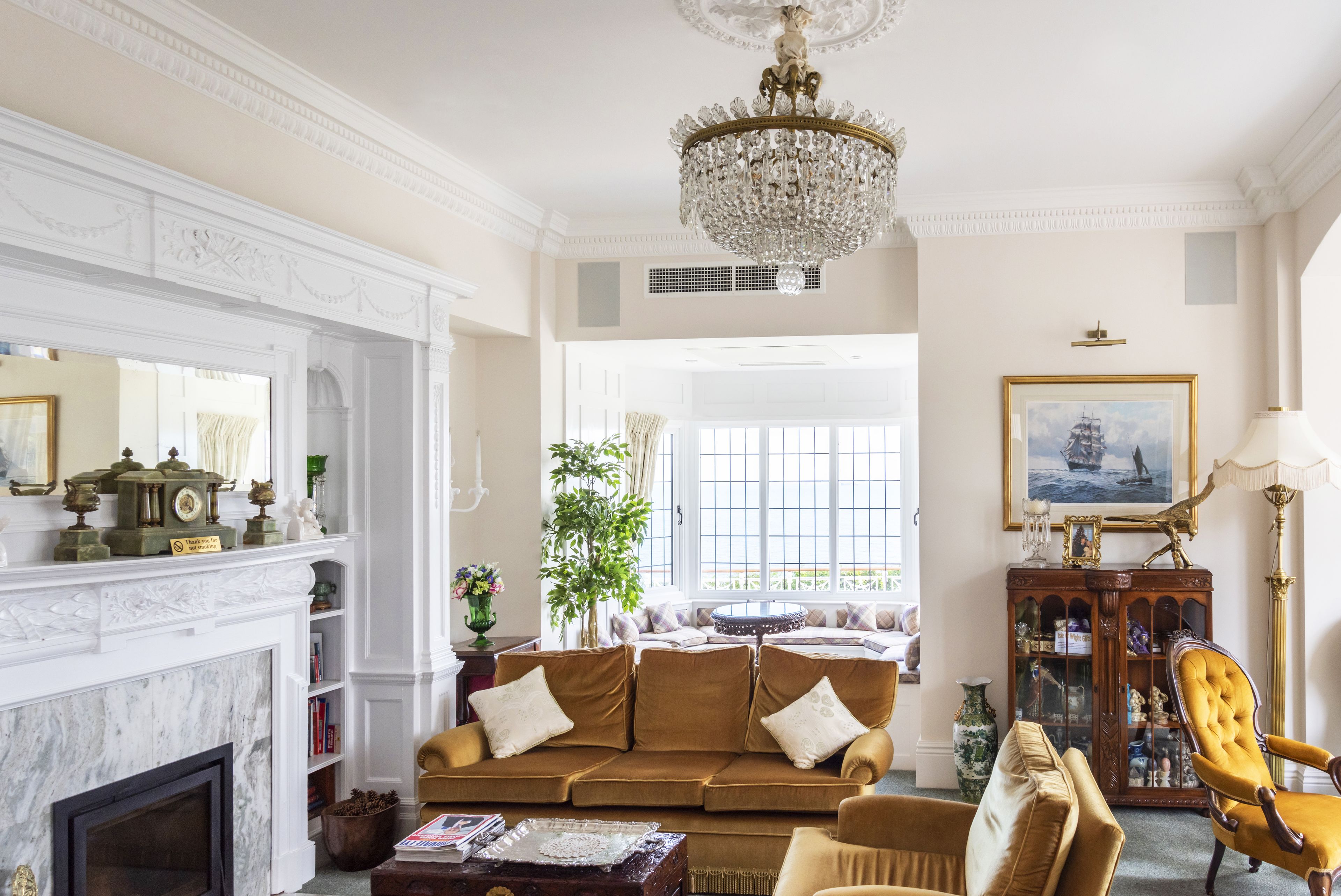 A classic living room with a fireplace, a chandelier, and a large window.
