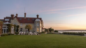 Un grand bâtiment à étages, doté d’un toit recouvert de tuiles rouges, d’une pelouse bien entretenue et offrant une vue sur la mer en arrière-plan.