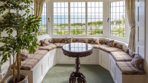 Un coin salon avec des sièges disposés en cercle autour d’une table ronde, une plante en pot et une vue sur la mer.