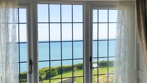 Une vue à travers une fenêtre à carreaux, donnant sur un jardin aménagé et la mer.