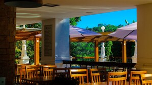 An outdoor dining area with wooden tables and chairs, covered by umbrellas, and a view of greenery. - Terra dos Diamantes (Lençóis)