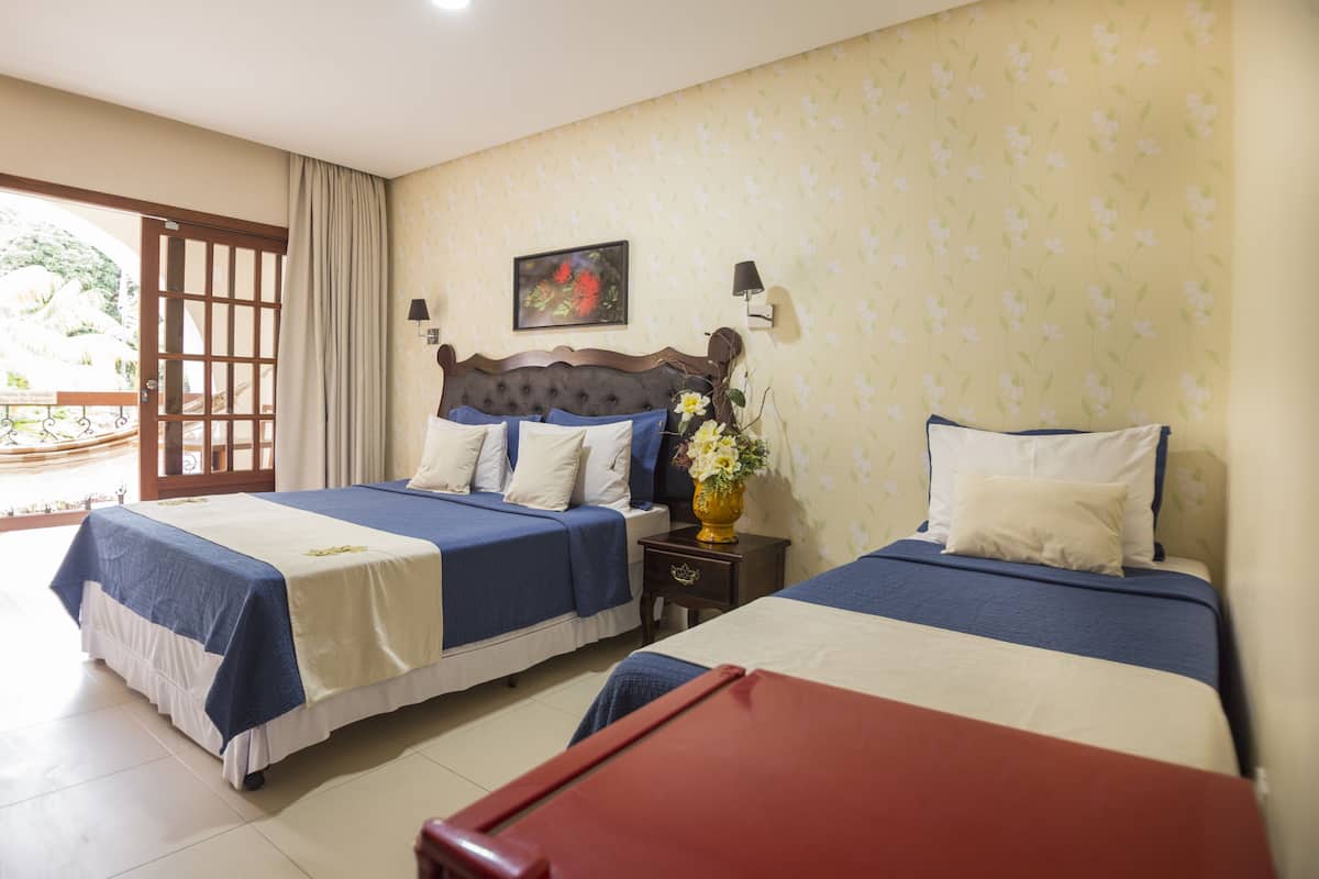 A hotel room with two beds, a wooden headboard, a nightstand, a vase with flowers, and a painting on the wall.