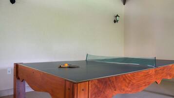 Une table de ping-pong dotée d’un cadre en bois et d’une surface de jeu verte, placée dans une pièce aux murs blancs et équipée de deux lampes fixées au mur.