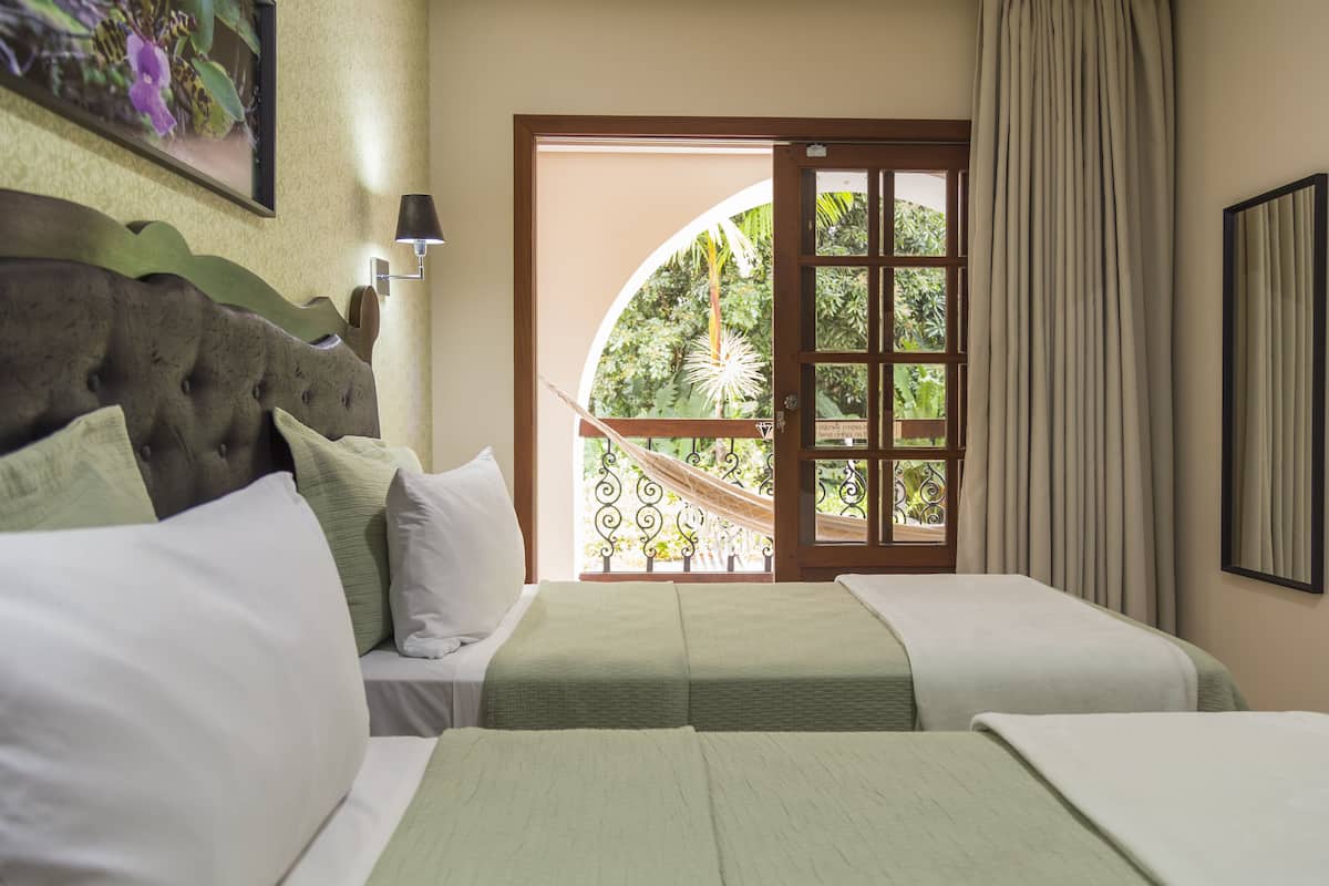 A hotel room with two beds, a view of a garden through a glass door, and a framed picture on the wall.